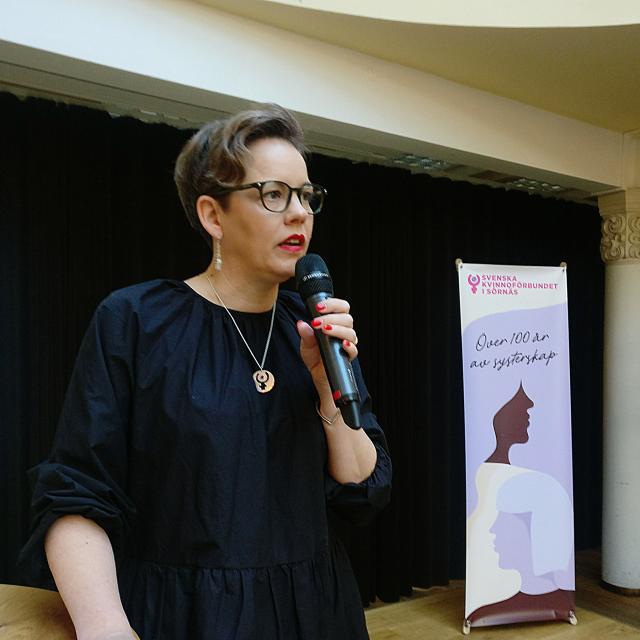 Pia Sundell står på en scen bredvid Sörnäs KF roll-up och talar i mikrofon.
