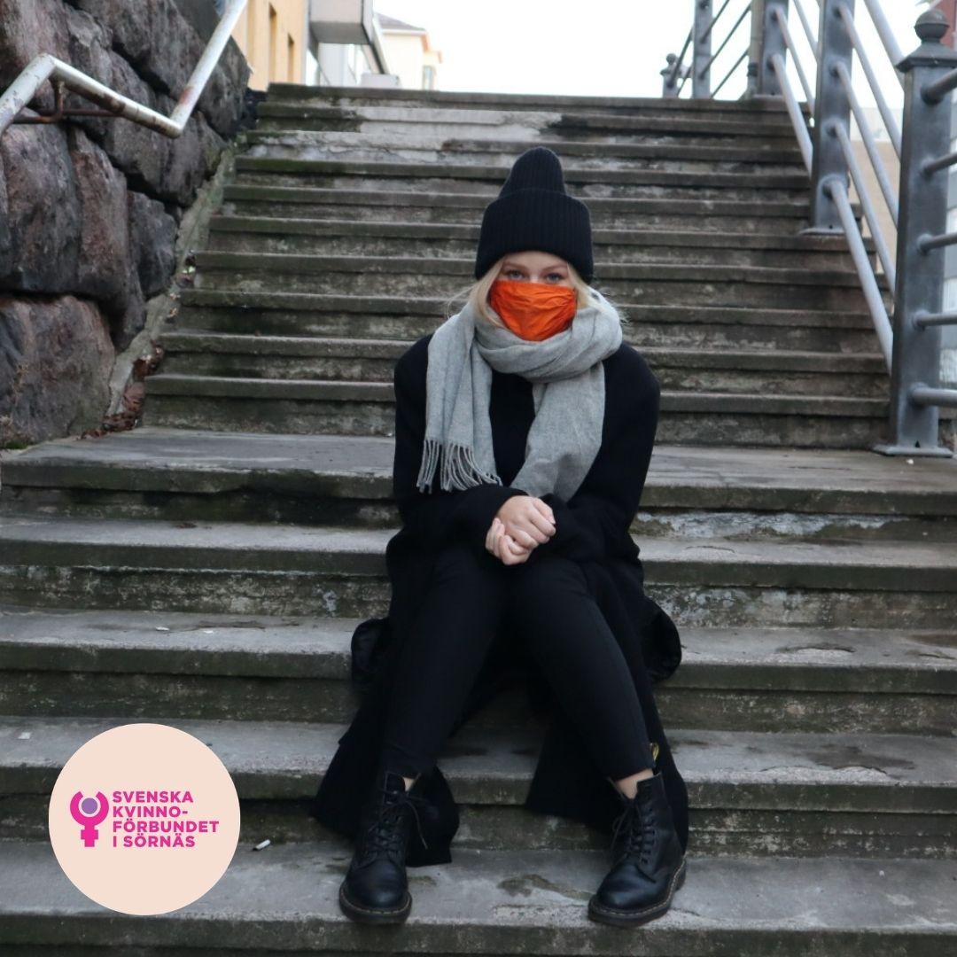Emmi med orange munskydd i urban miljö.